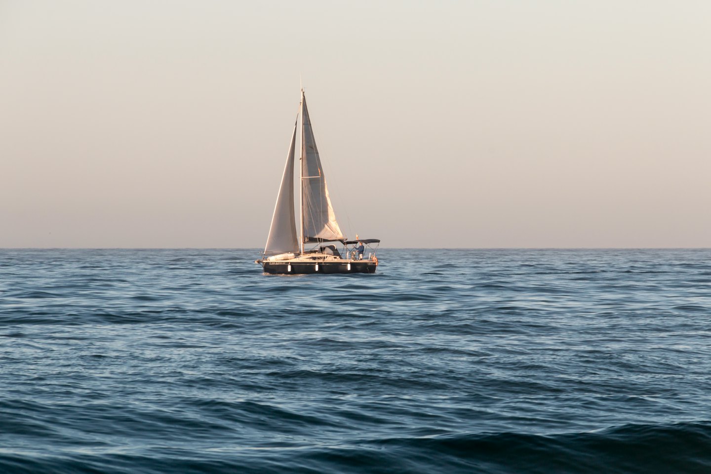 Una barca a vela con vele bianche naviga su acque oceaniche calme.