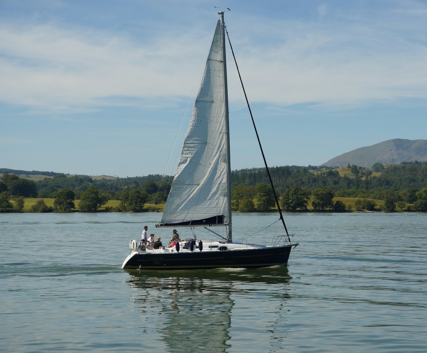 Una barca a vela scivola sull'acqua vicino a colline alberate.